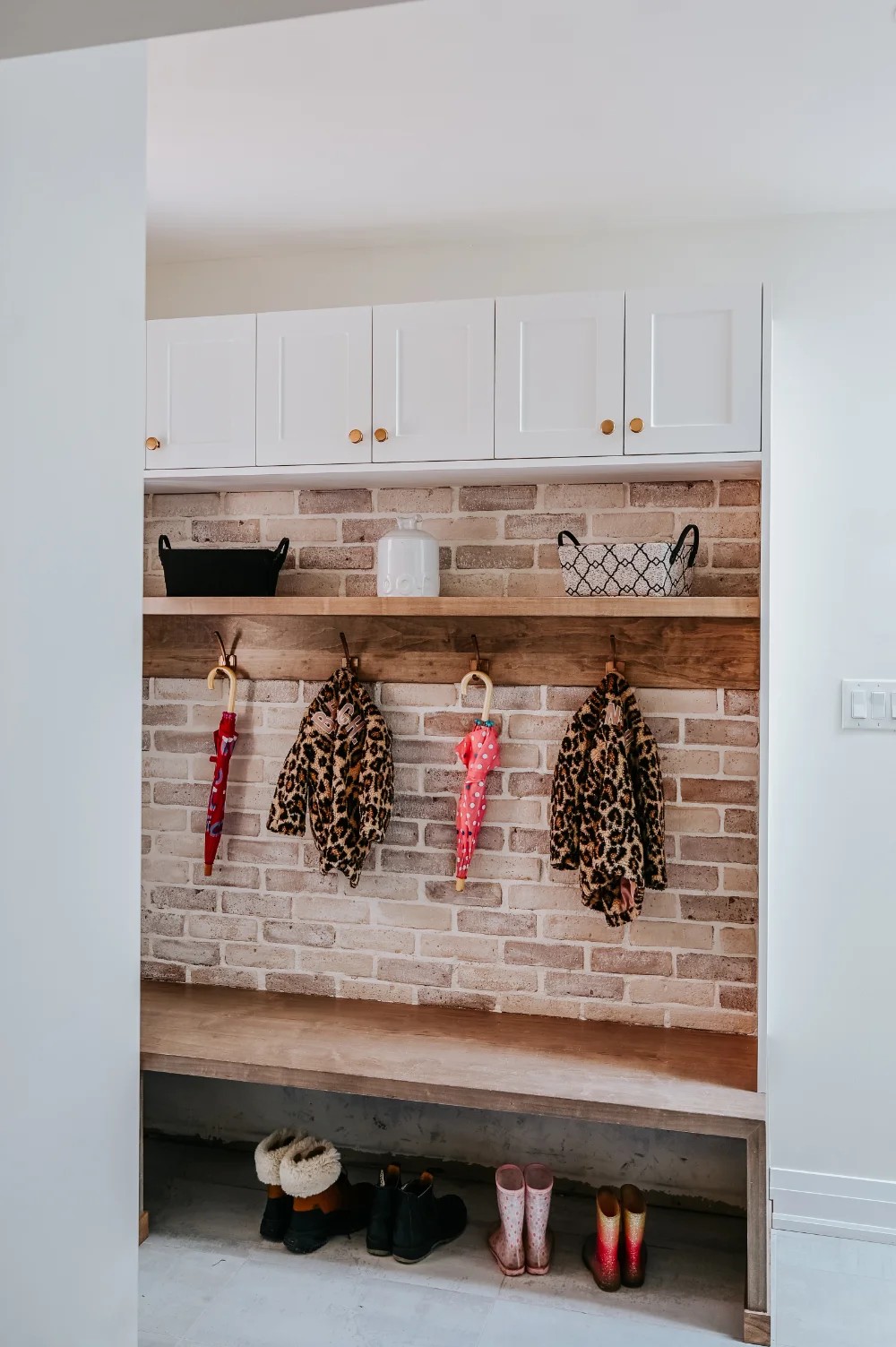 Entryway with boots lined up under a bench and coats hanging on hooks